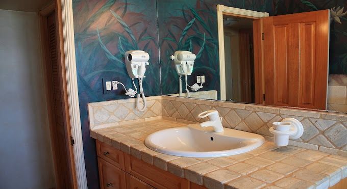 A bathroom with a sink , mirror and hair dryers.