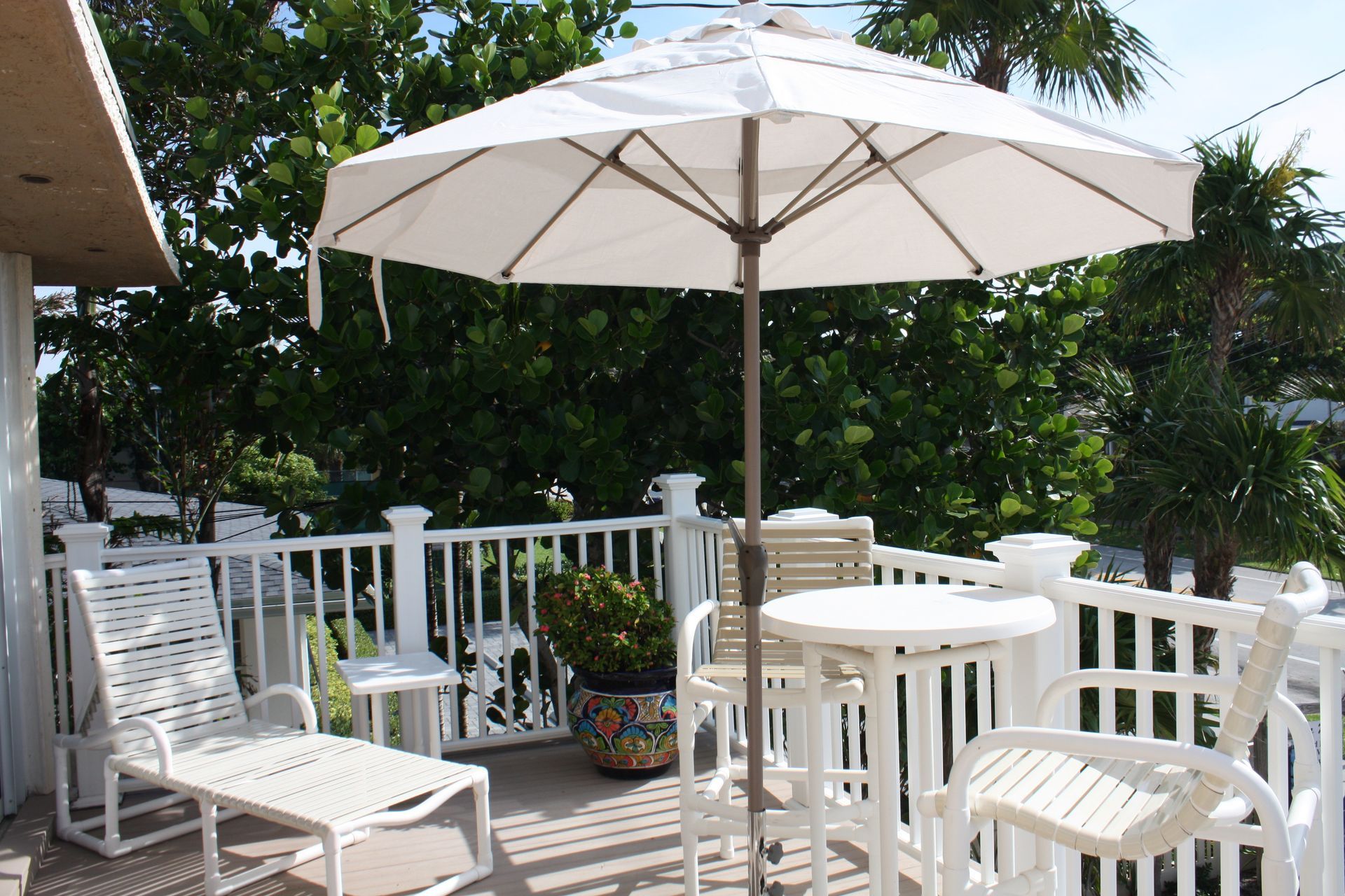 A white umbrella is sitting on a deck with chairs and a table