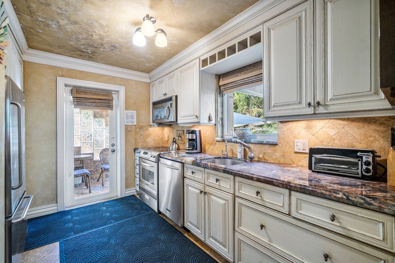 A kitchen with white cabinets , granite counter tops , stainless steel appliances and a blue rug.
