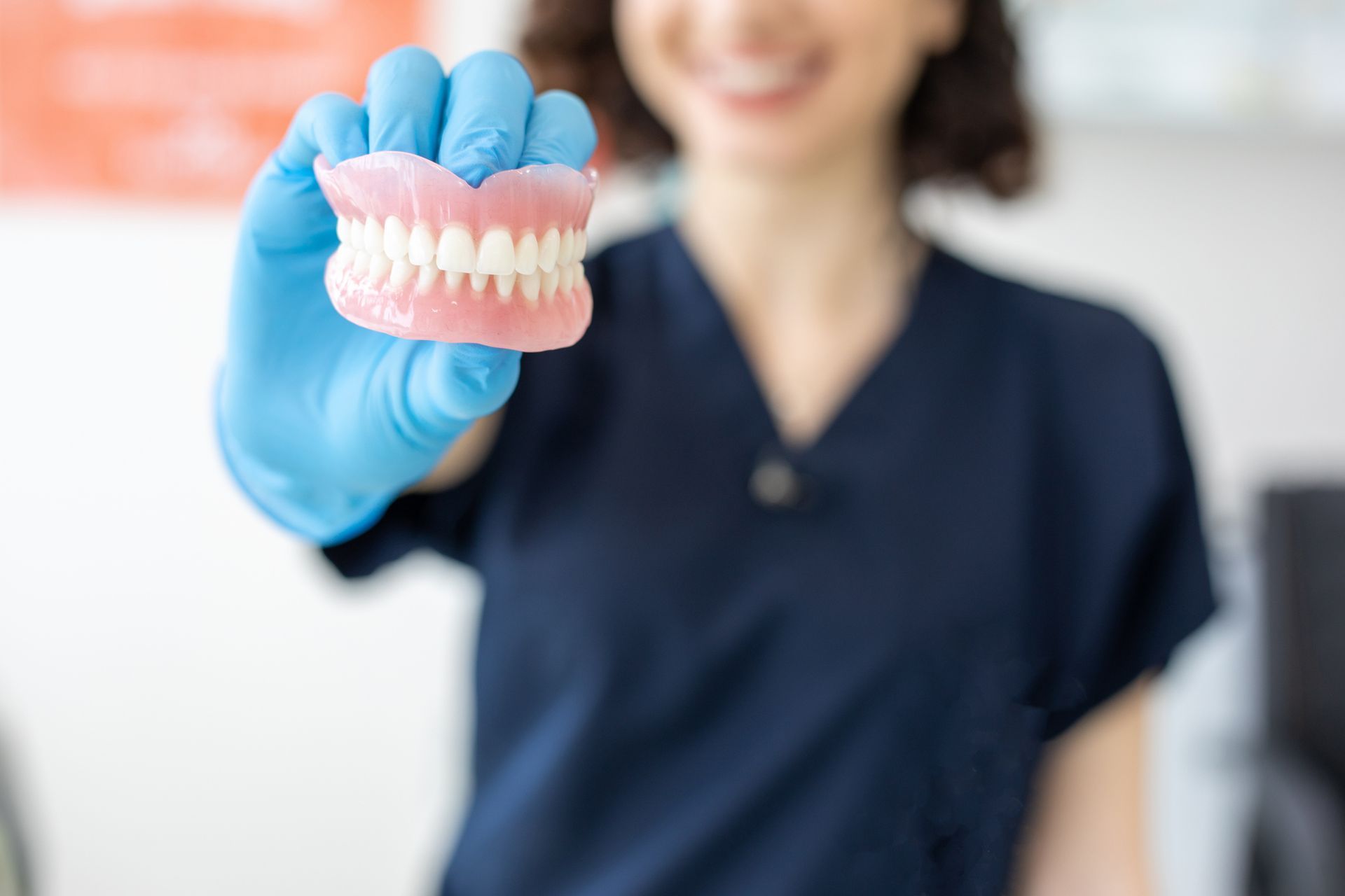 Dentist holding dentures, smiling, wearing blue scrubs and gloves.