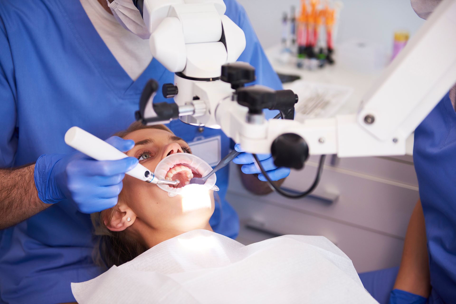 Dentist examining patient's mouth with a microscope, using tools, in dental clinic.