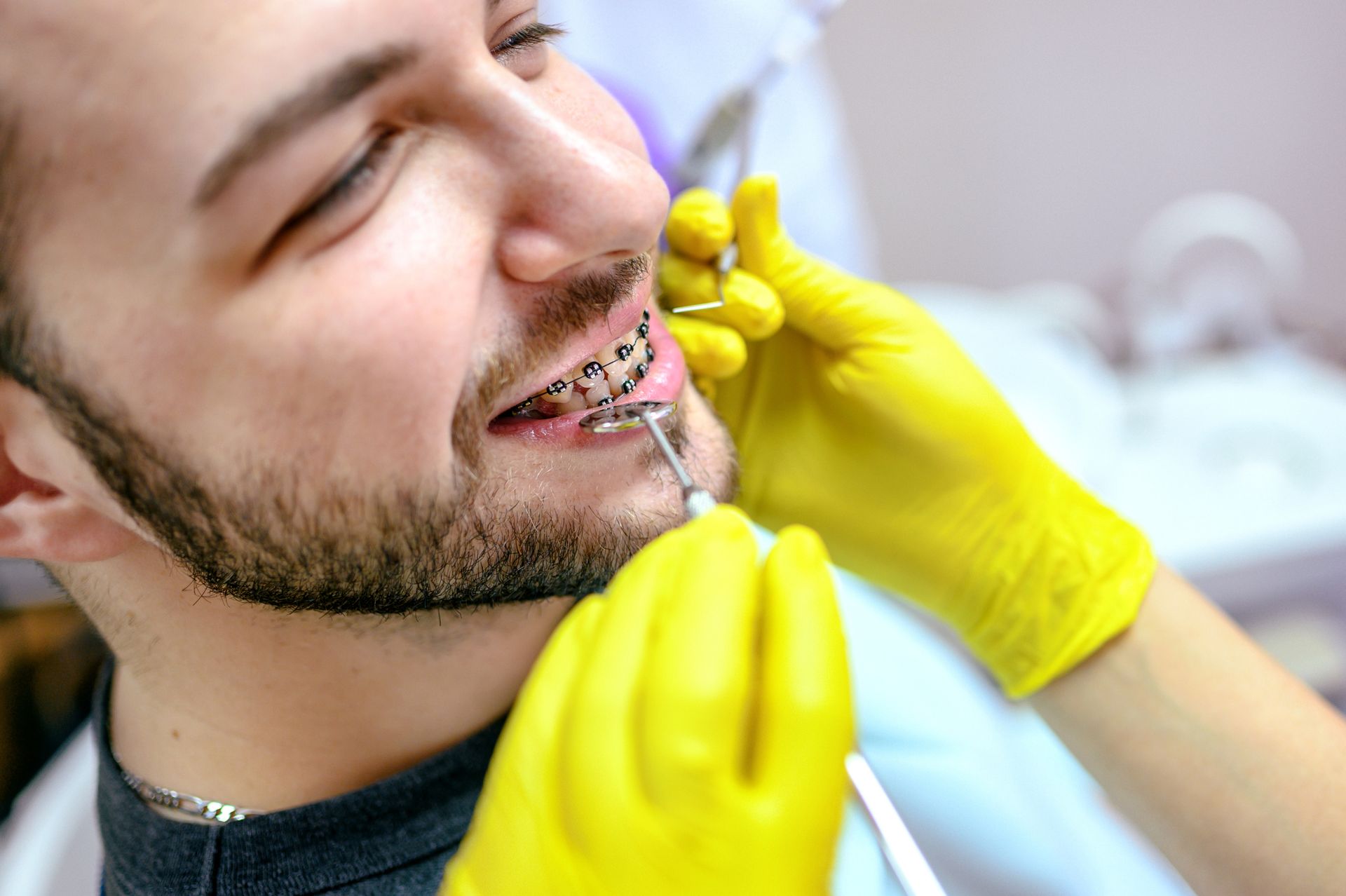 Man with braces has dental work done by someone wearing yellow gloves.