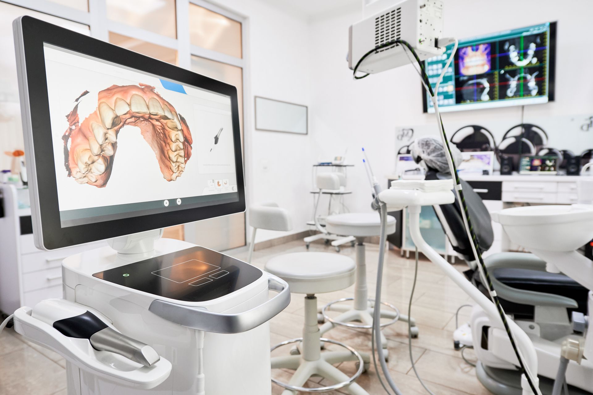 Dental office interior: a digital scan of teeth displayed on a large monitor, with dental chair and equipment.