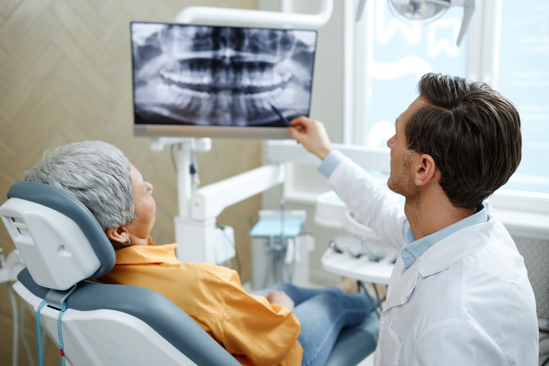Dentist pointing at an X-ray on a screen, explaining it to a patient in a dental chair.