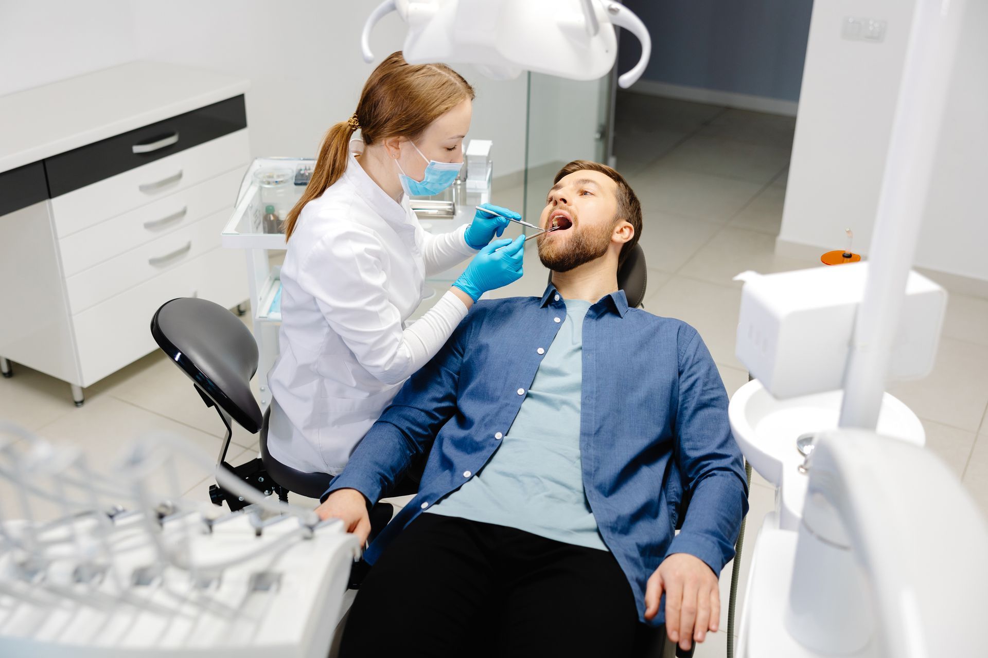 Dentist examining a man's teeth in a dental office. Dentist wears a mask and gloves.