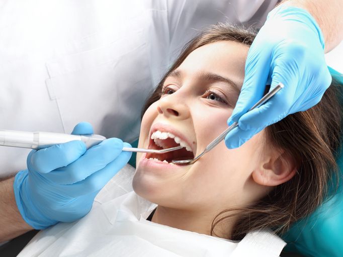 Girl at the dentist with mouth open, being examined. Dentist in blue gloves holds tools.