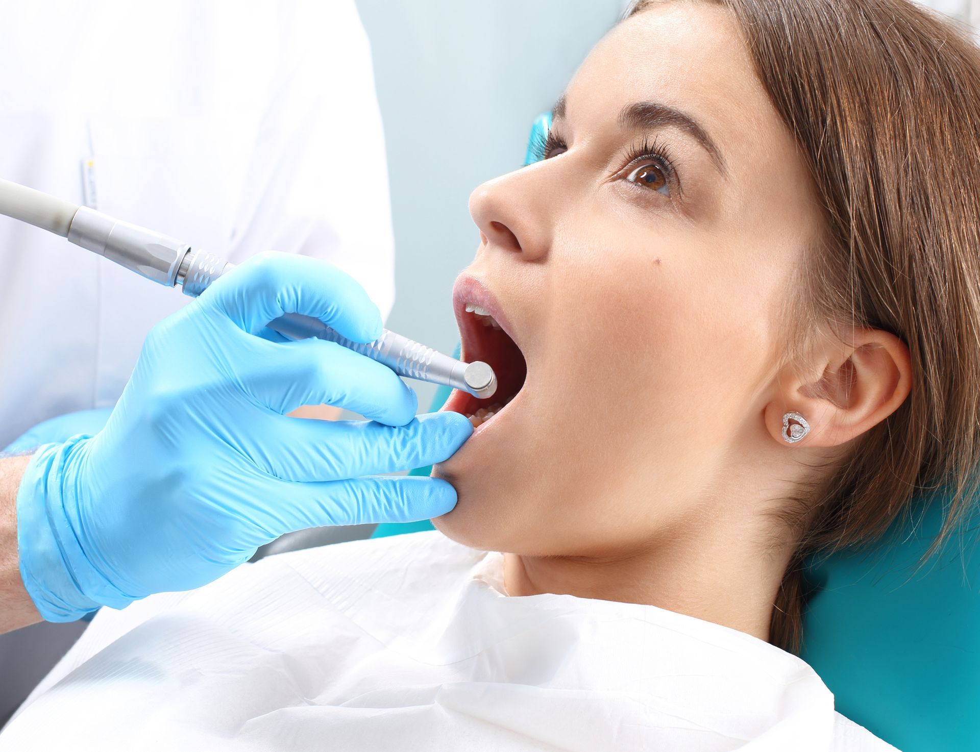 Woman at dentist, mouth open, being examined with tools by gloved hand.