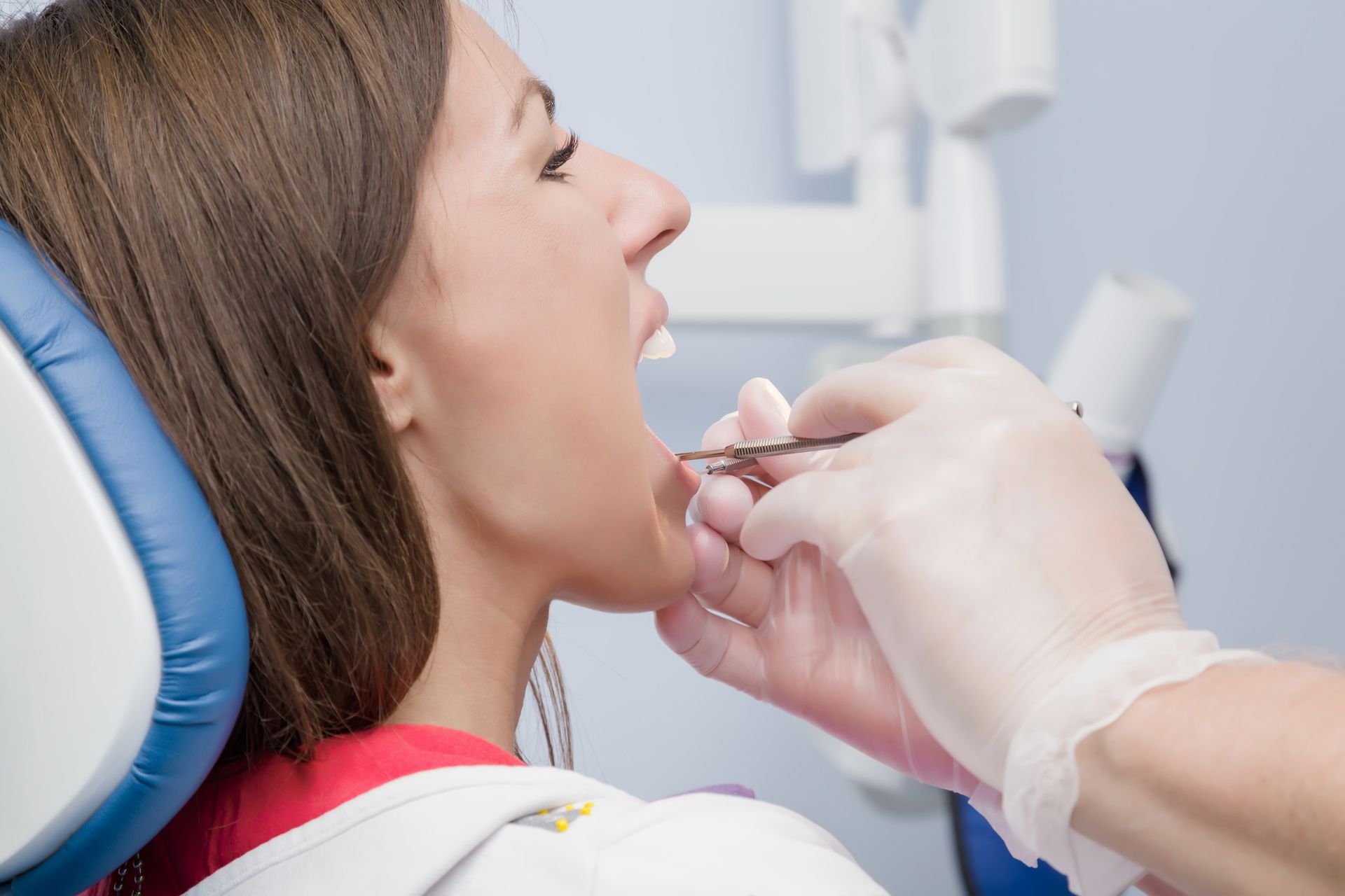 Woman in dentist chair, mouth open, being examined by gloved hand with dental tools.