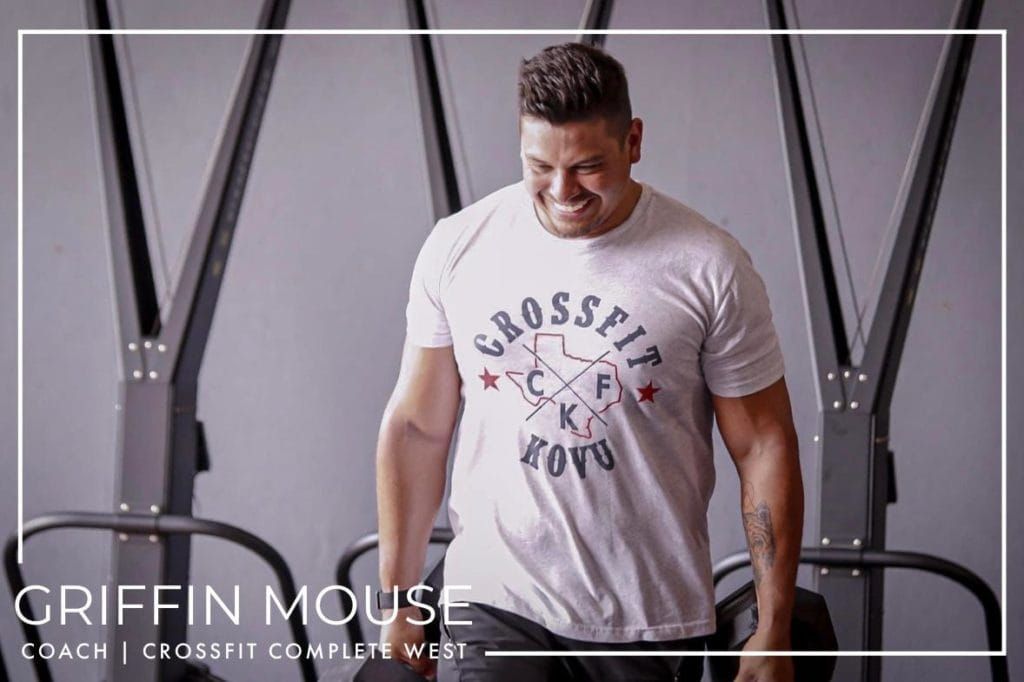 A man wearing a crossfit t-shirt is standing in a gym.