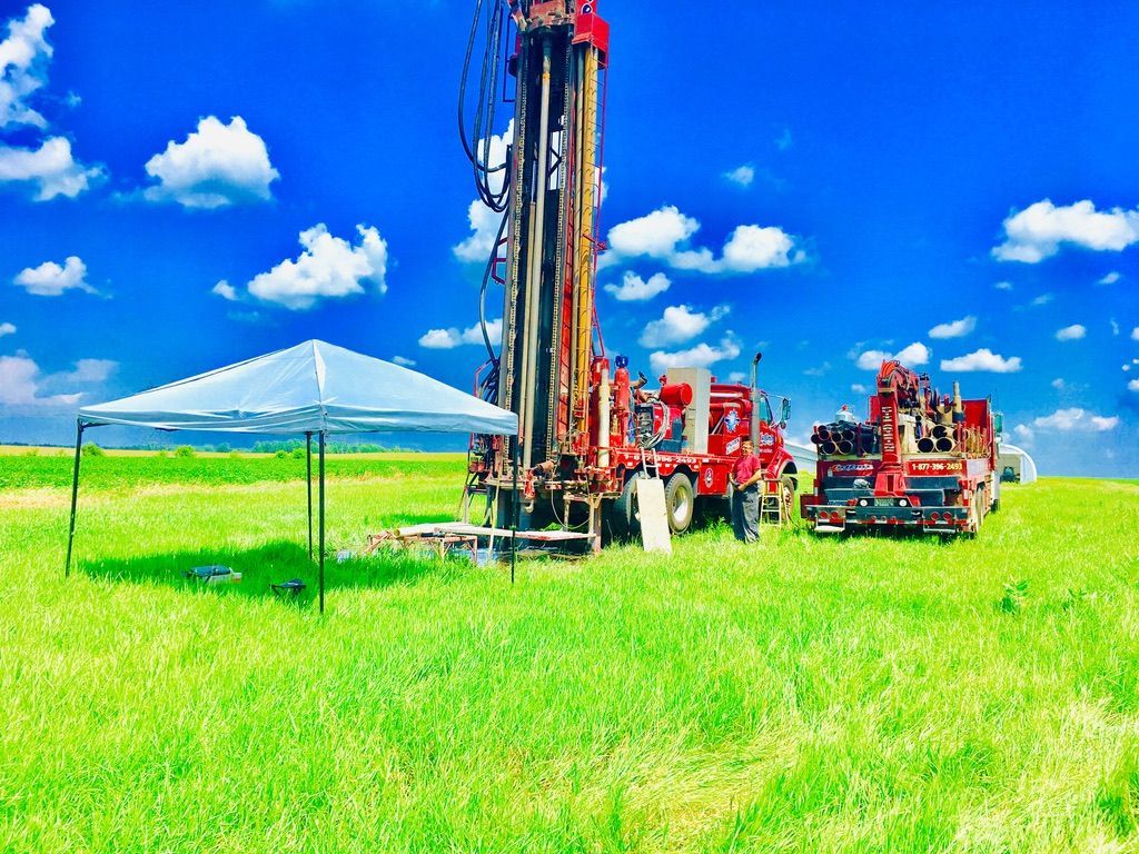 Plateforme de forage dans un champ verdoyant sous un ciel bleu nuageux, à côté d'une tente blanche.