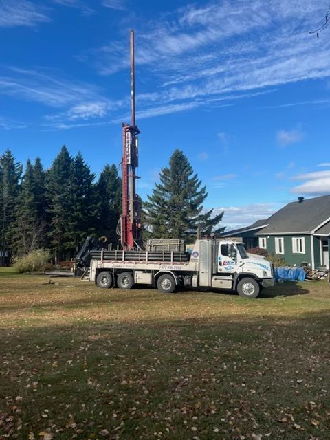 Un camion-foreuse installé sur une pelouse près d'une maison, se prépare à forer un puits par une journée ensoleillée.