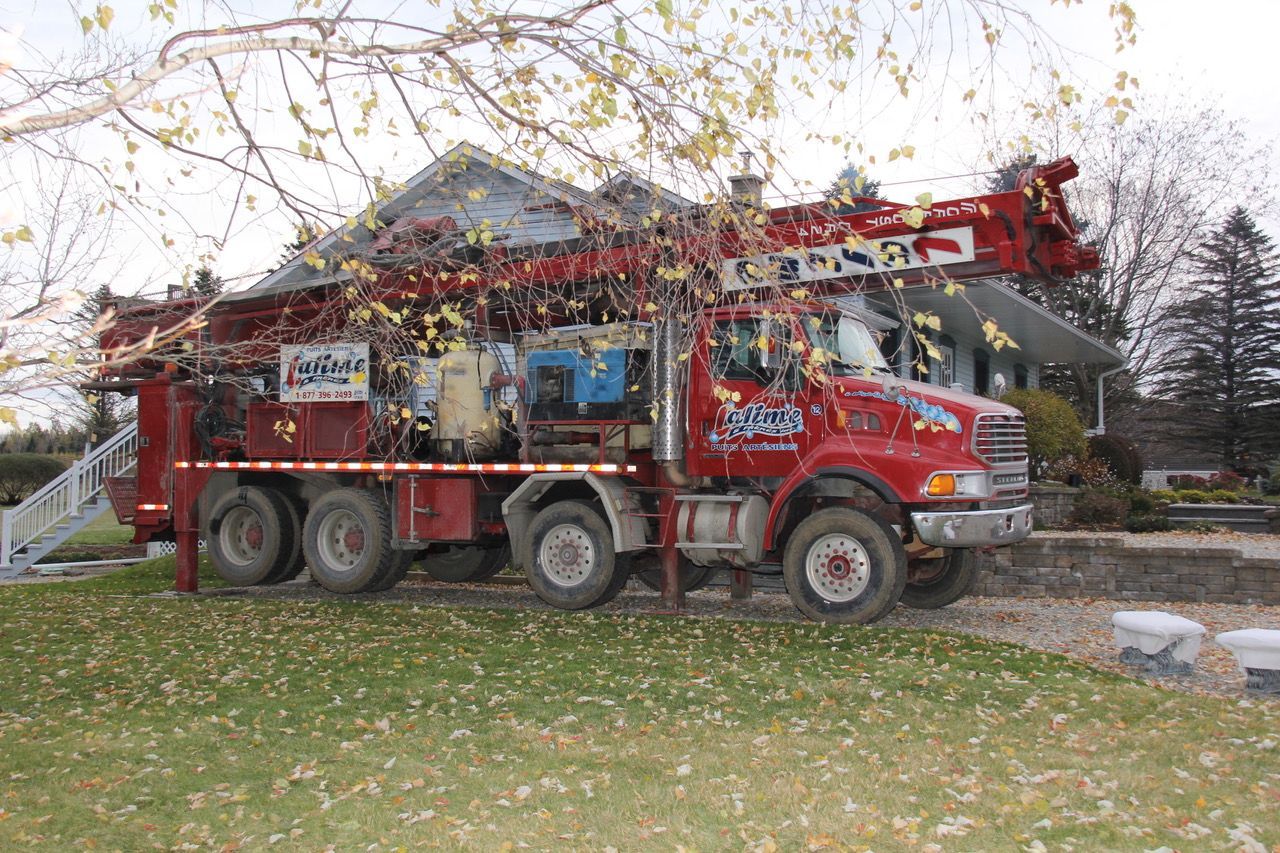 Camion de forage de puits rouge stationné près d'une maison, bras rouge tendu vers le haut.