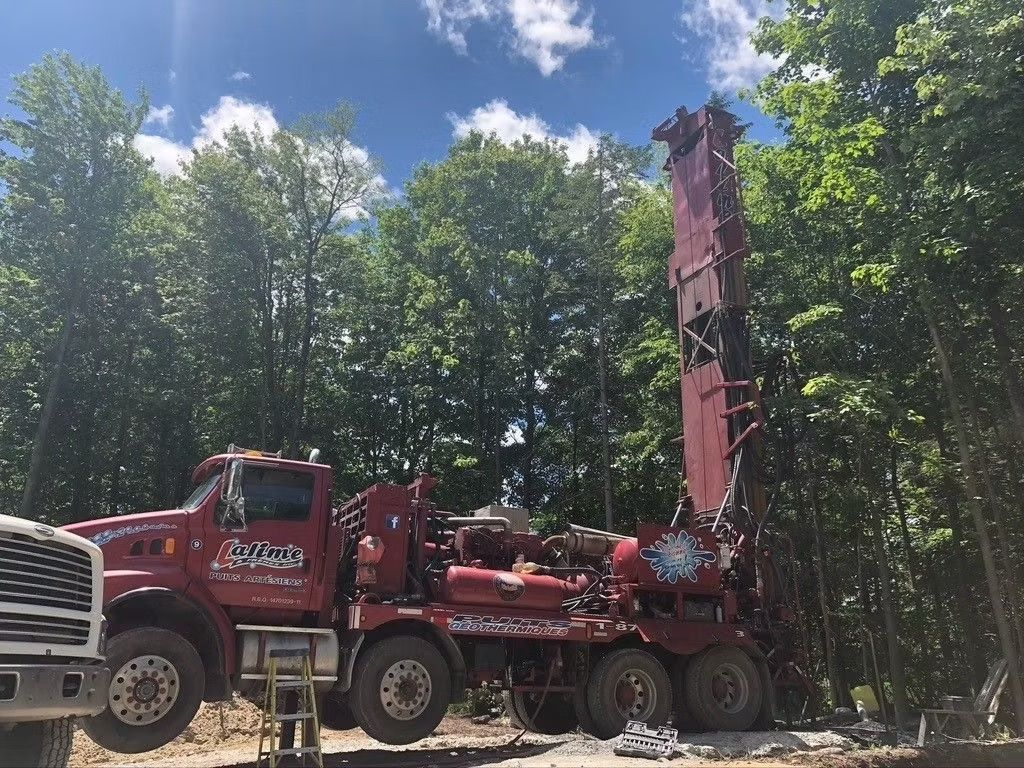 Plateforme de forage rouge dans une zone boisée sous un ciel bleu.