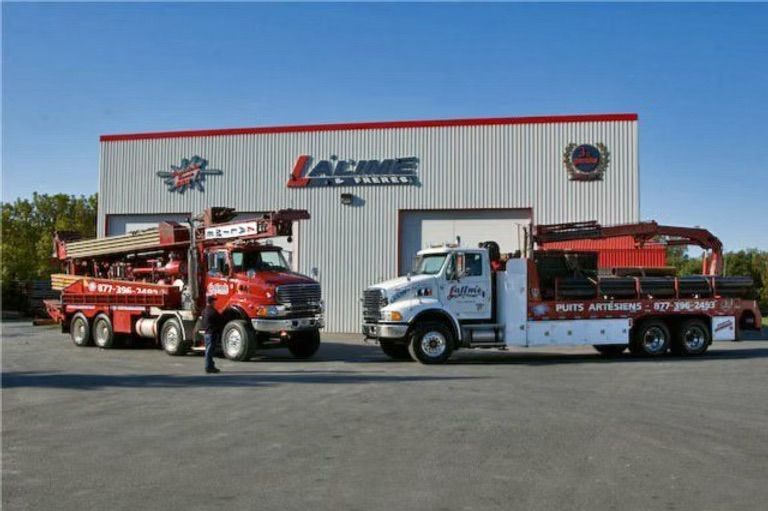 Deux camions Acme stationnés devant un bâtiment blanc arborant le logo et le nom de l'entreprise, sous un ciel bleu.