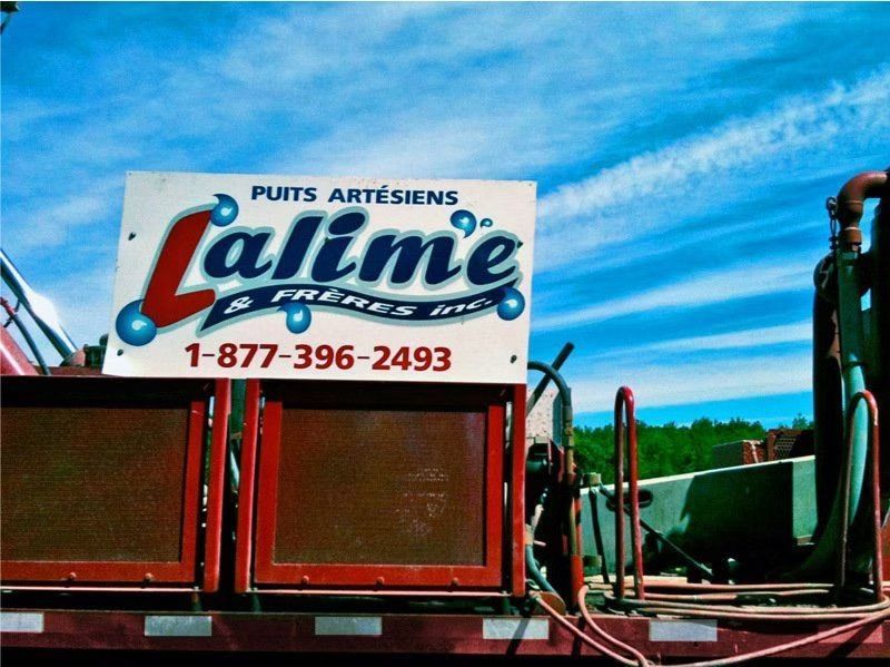 Panneau pour « Lalime & Frères Inc. Puits Artisans » avec le numéro de téléphone 1-877-396-2493, monté sur la benne d'un camion rouge sur fond de ciel bleu.