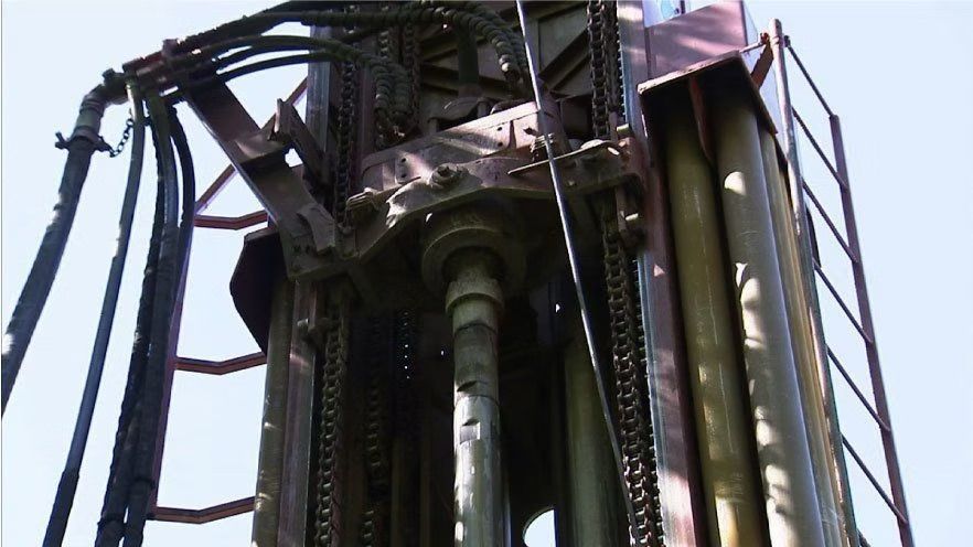 Gros plan sur une installation de forage, montrant des composants métalliques, des tuyaux et des conduites hydrauliques, sur fond de ciel lumineux.