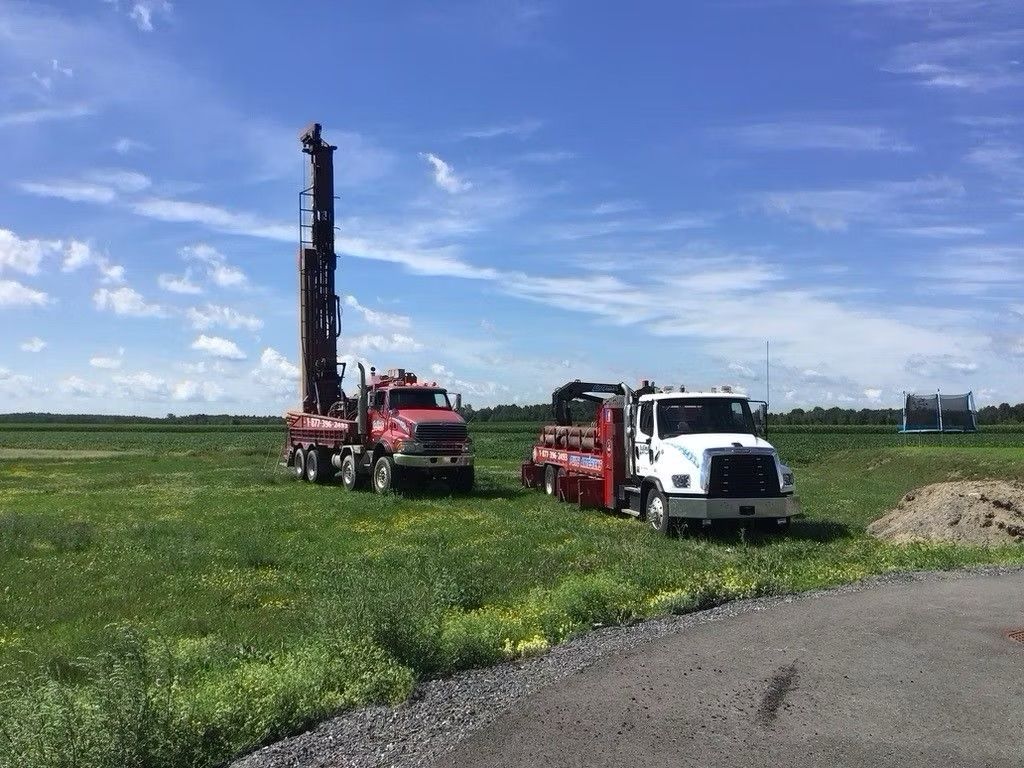 Deux camions de forage sur un champ herbeux sous un ciel d'un bleu éclatant.