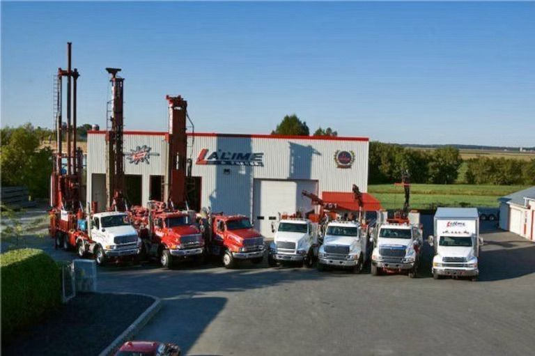 Une rangée de camions de forage et de service est garée devant un entrepôt blanc ; ciel bleu.