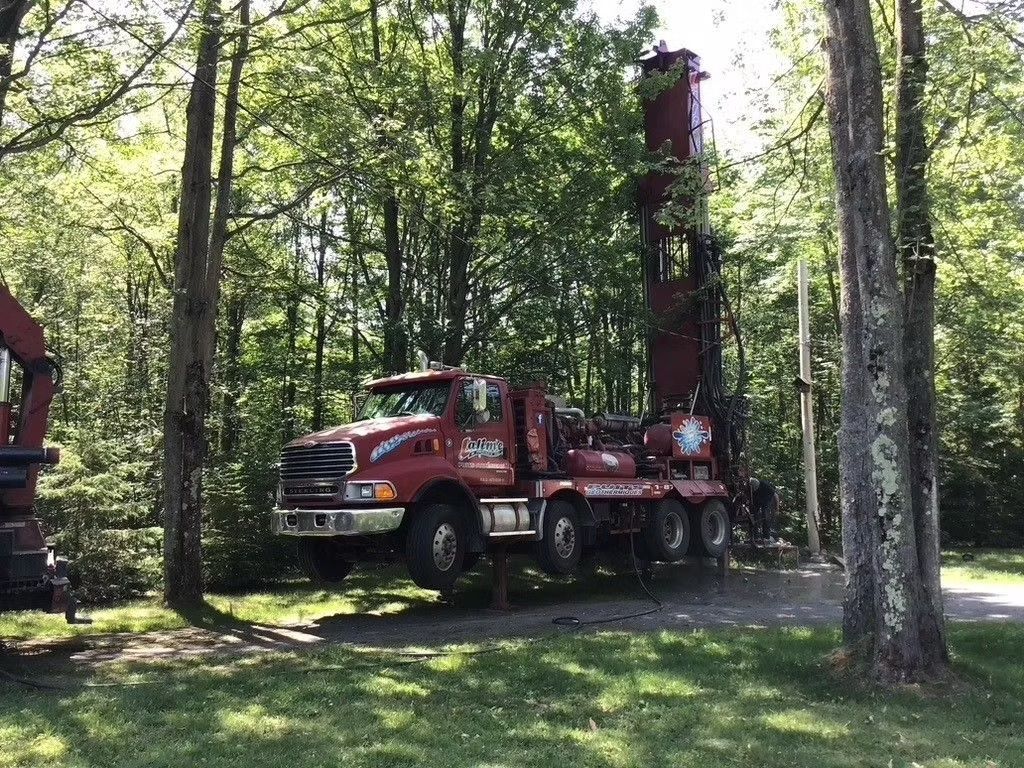 Camion de forage rouge dans une zone boisée.