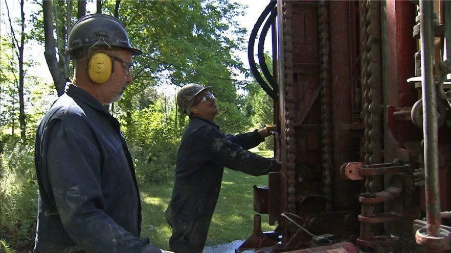 Deux ouvriers utilisent du matériel de forage à l'extérieur. L'un d'eux porte une protection auditive.