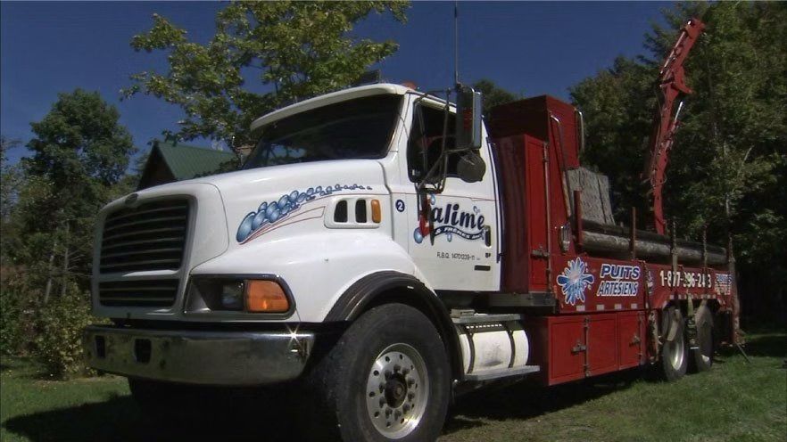 Un camion grumier blanc et rouge est stationné à l'extérieur sous un ciel bleu, avec des arbres en arrière-plan.