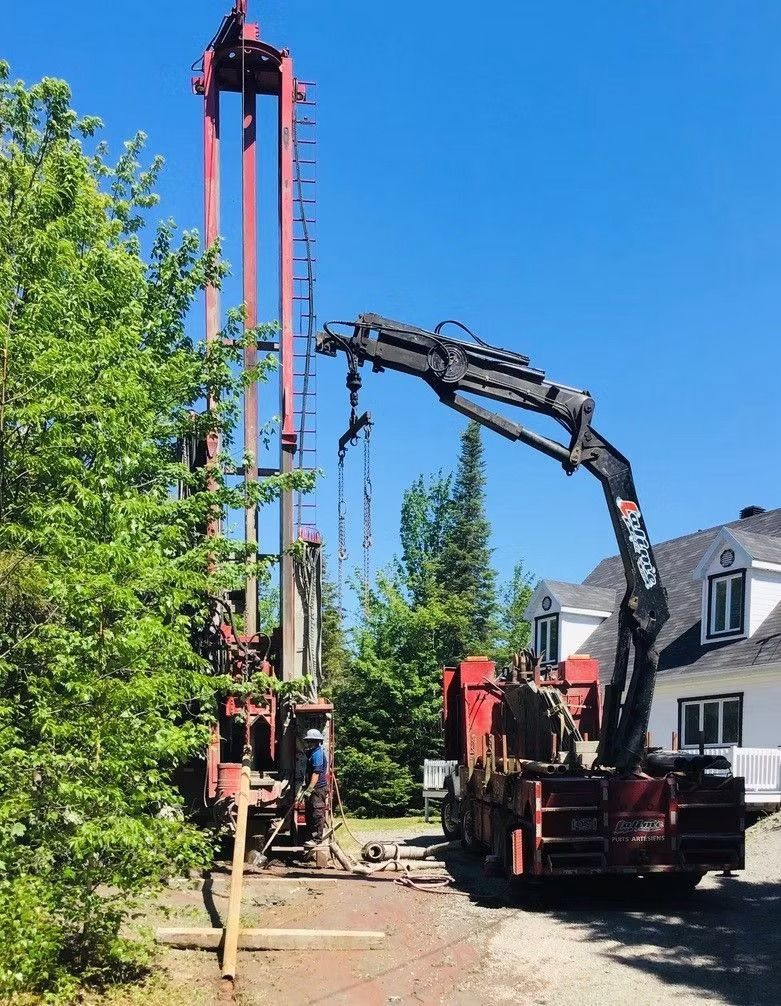 Une foreuse rouge à côté d'un arbre et d'une maison blanche, par une journée ensoleillée.