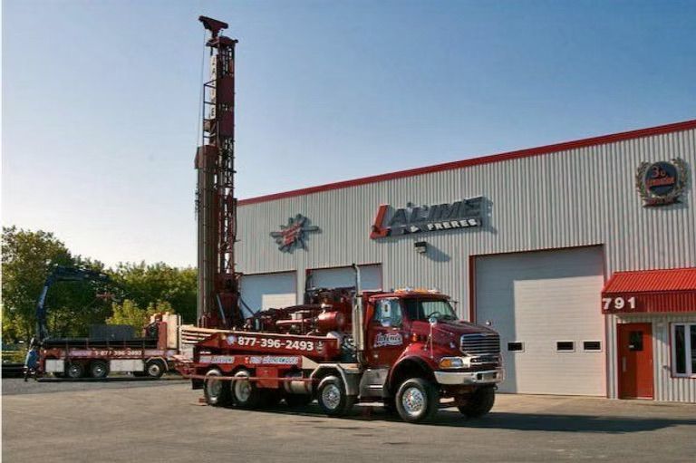 Camion de forage rouge devant un bâtiment portant l'enseigne « Jaime & Fils ».