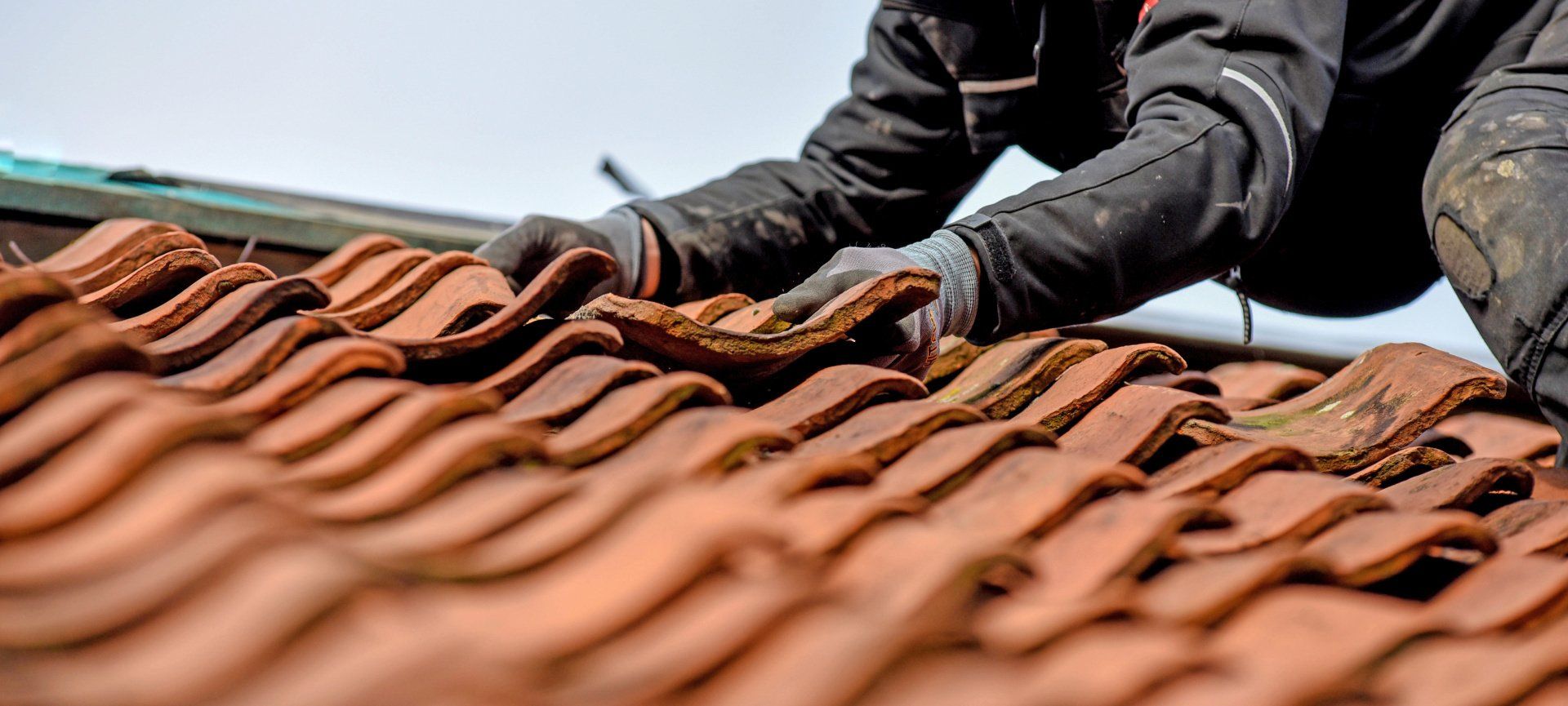 person on red tiled roof fixing tiles