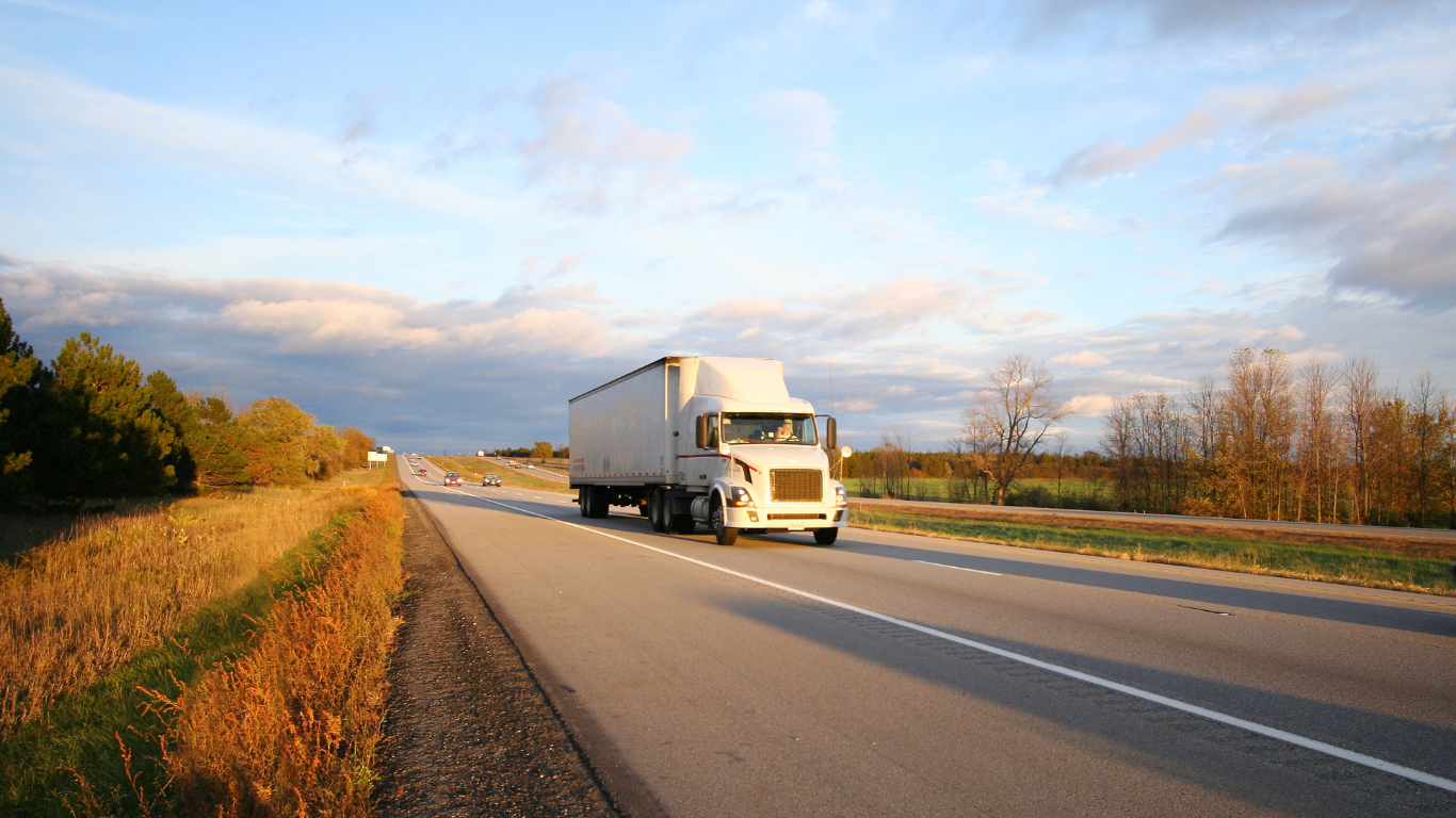 Semi-truck driving on highway at sunset.