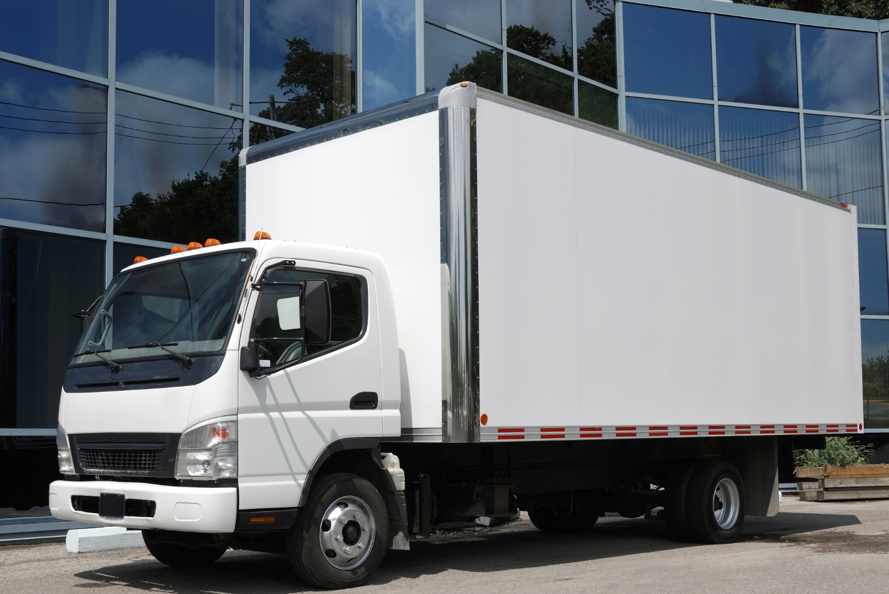 White box truck parked in front of a glass-walled building.