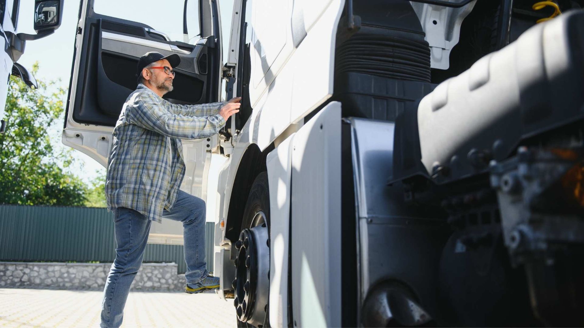 Man in a plaid shirt steps into the cab of a white semi-truck.