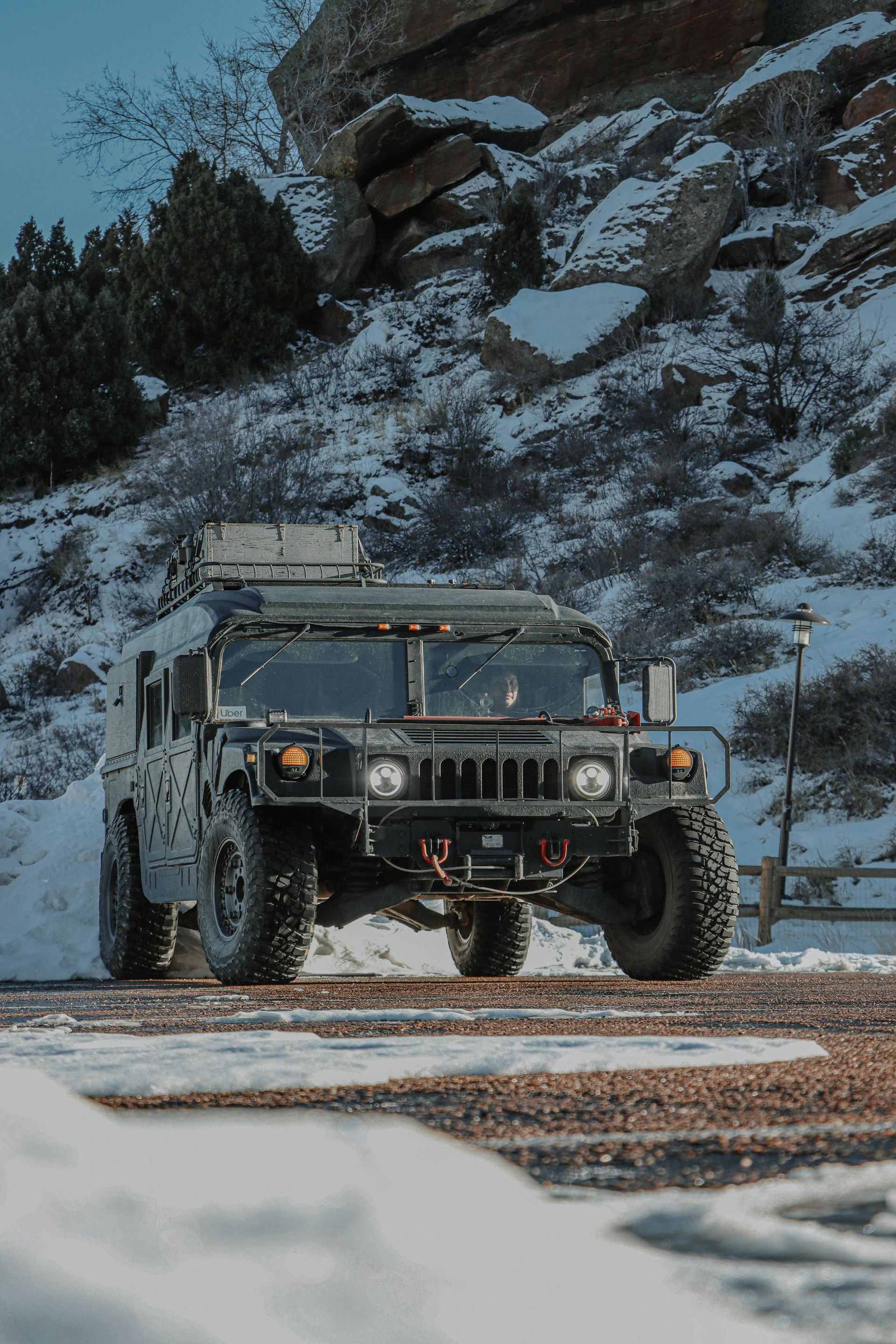 Black Humvee parked on a snowy road with rocky mountain backdrop.