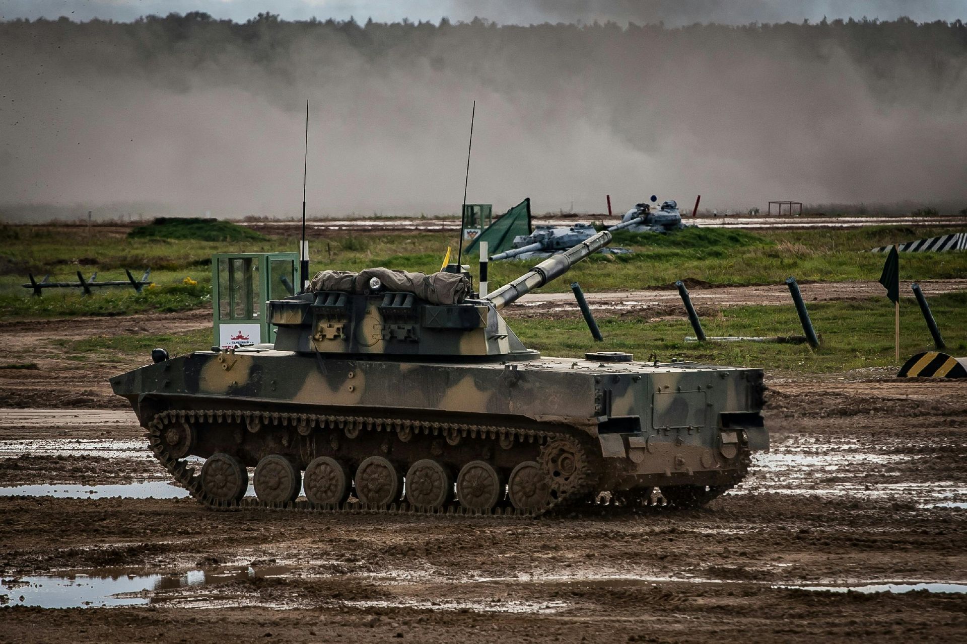 A camouflaged armored vehicle on a muddy field during an event.