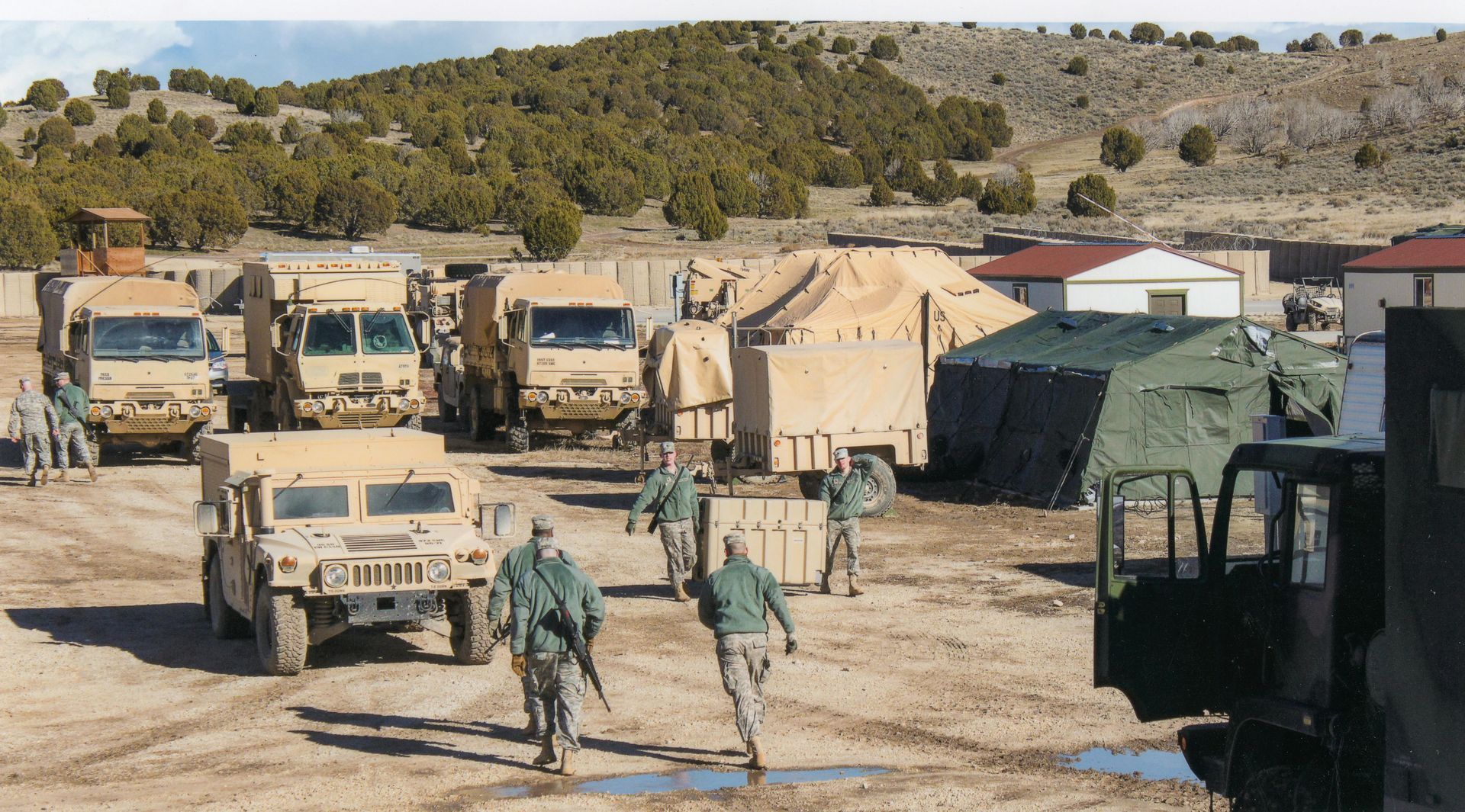 Soldiers walk past military vehicles and tents in a desert camp. links to operational solutions.