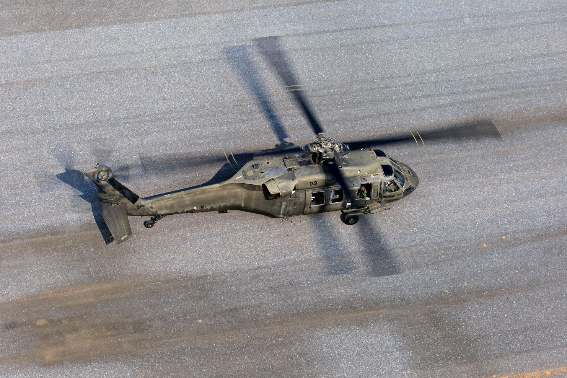 Black military helicopter on a gray surface with its blades spinning, casting a shadow.