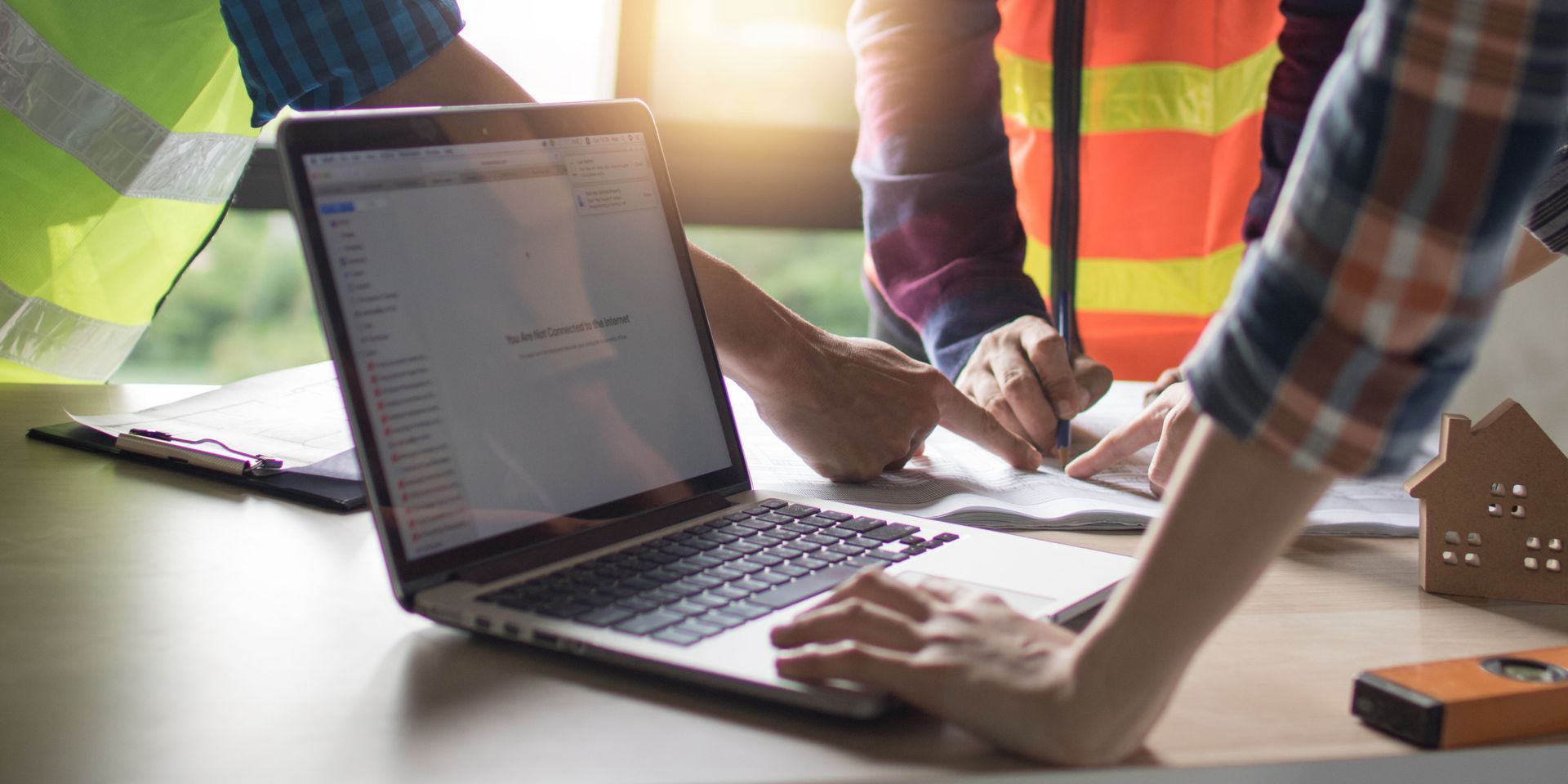 Three people review building plans, with a laptop and documents on a table.