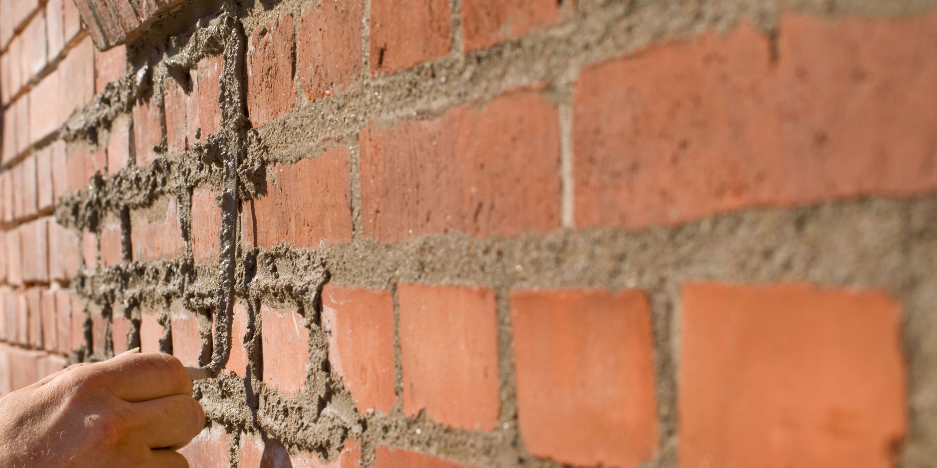Close-up of a brick wall with mortar repair. A hand reaches toward the wall.