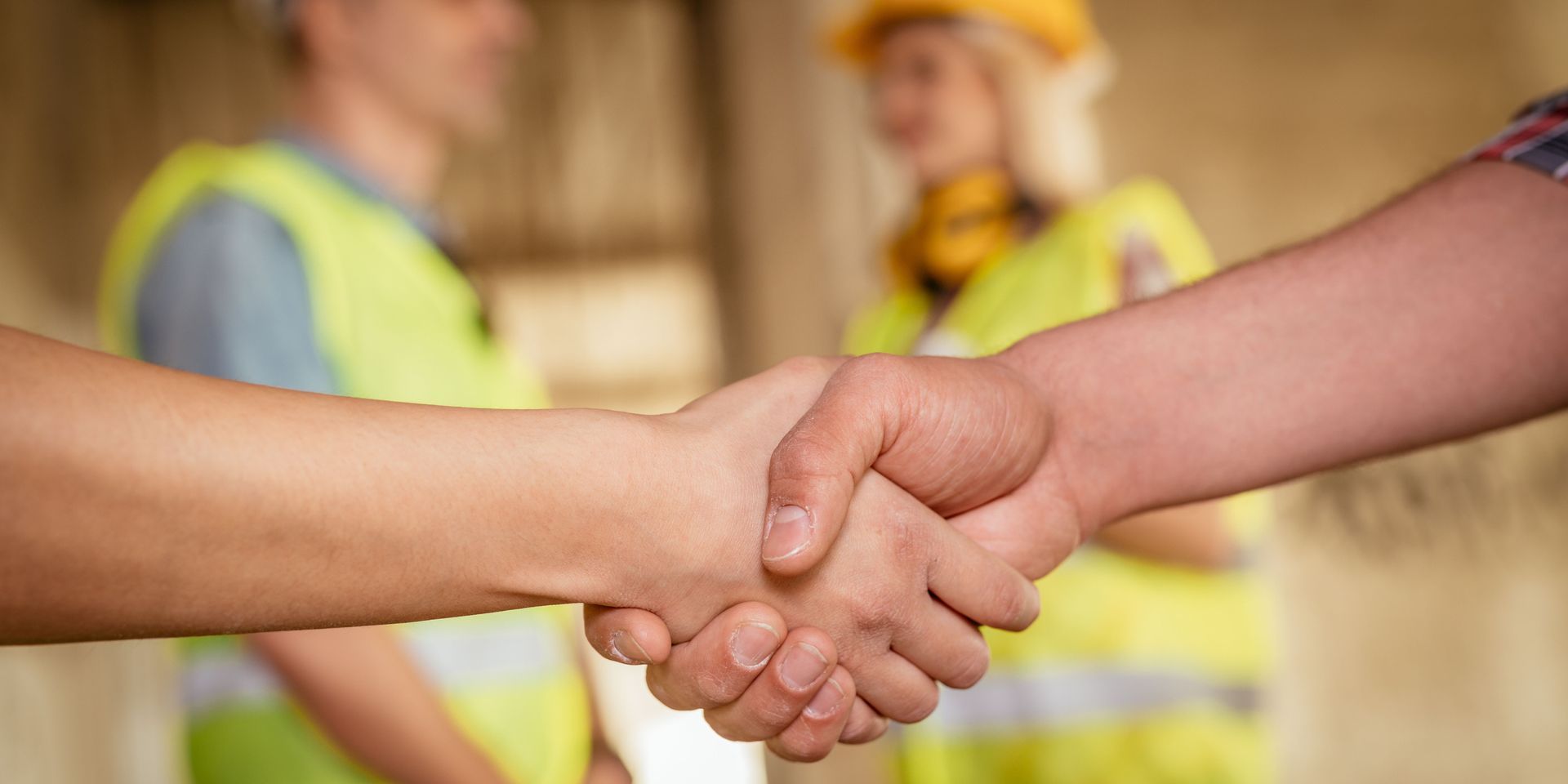 Construction workers shaking hands, a yellow vest and hardhat are visible in the background.
