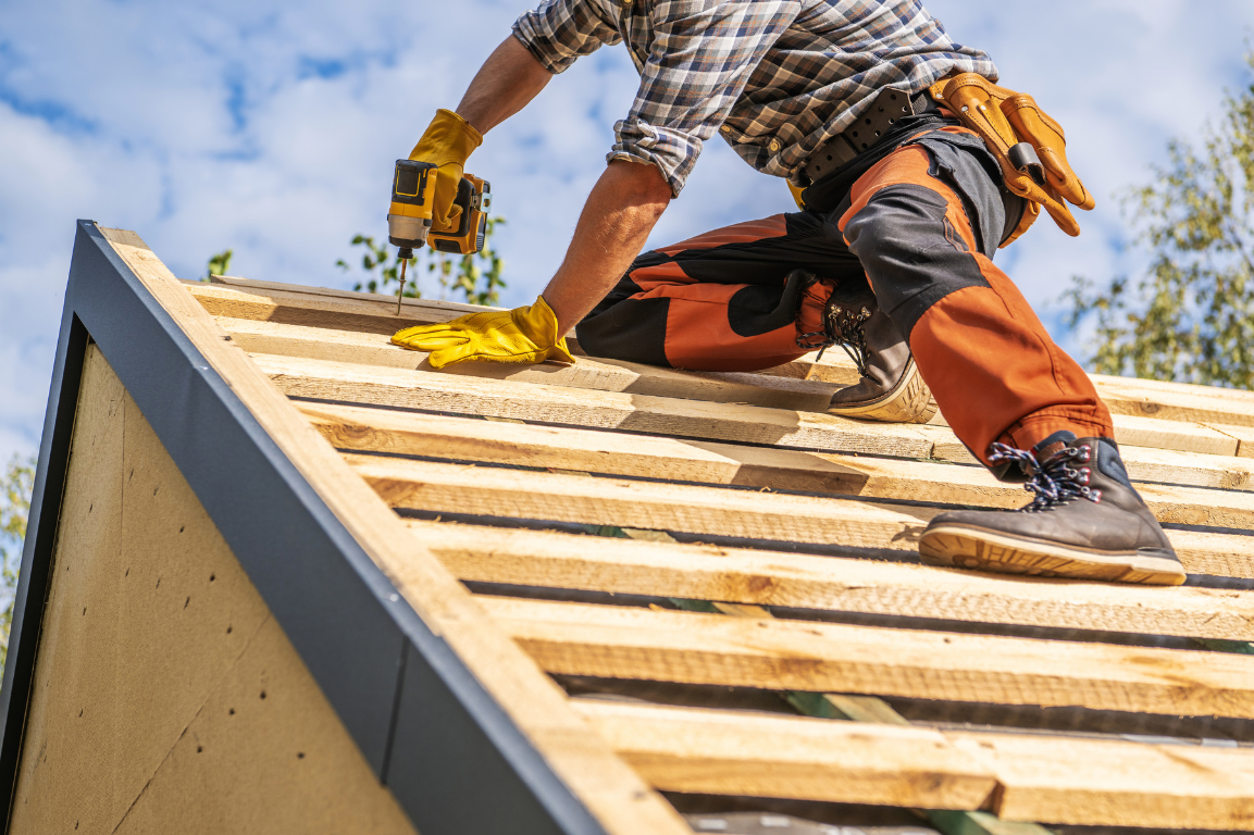A roofer is working on a wooden roof with a drill.