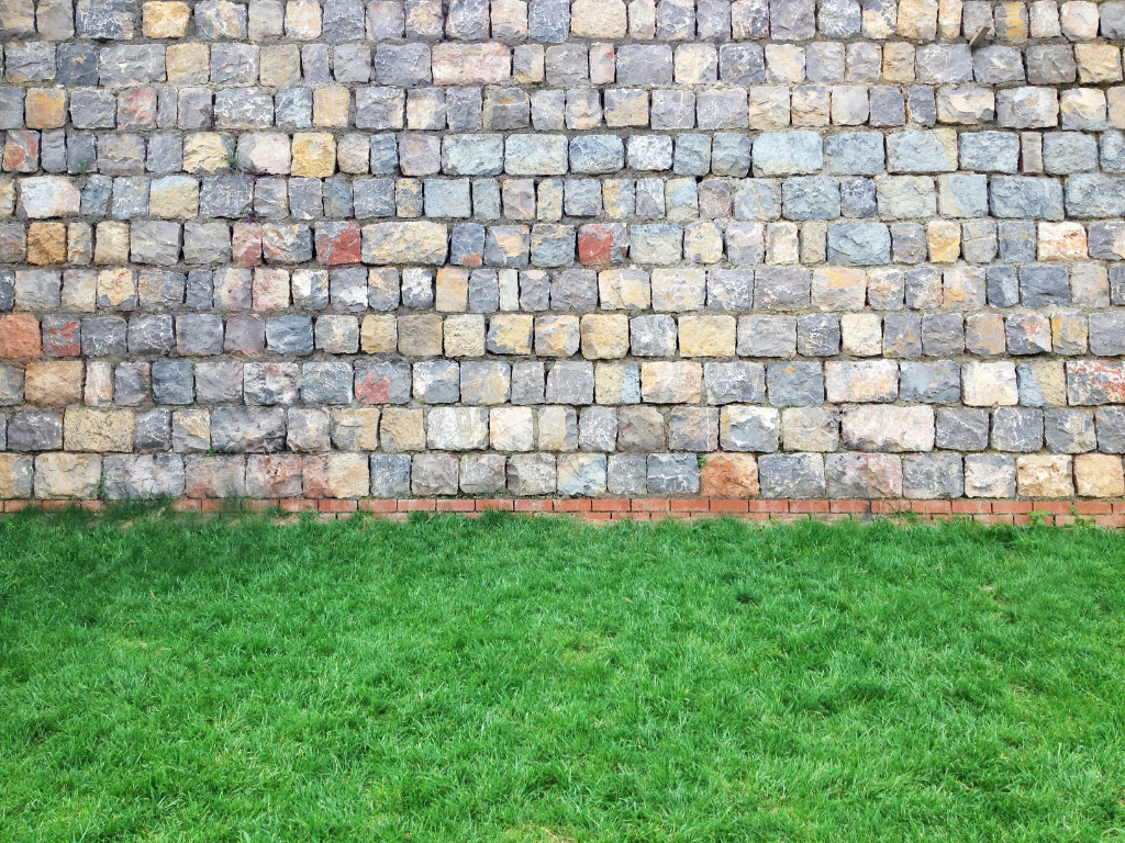 A brick wall with a lush green lawn in front of it.