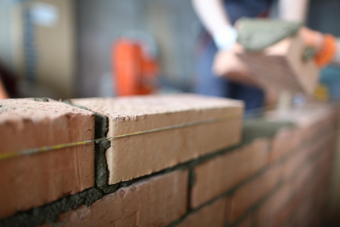 A builder is laying bricks on a brick wall.