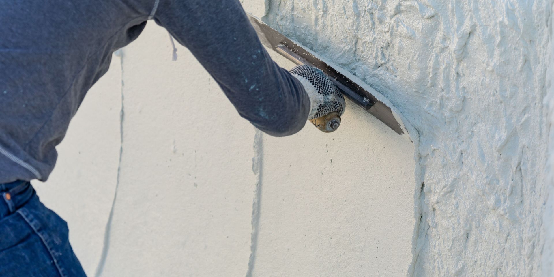 Person using a trowel to apply plaster to an outside corner of a light-colored wall.