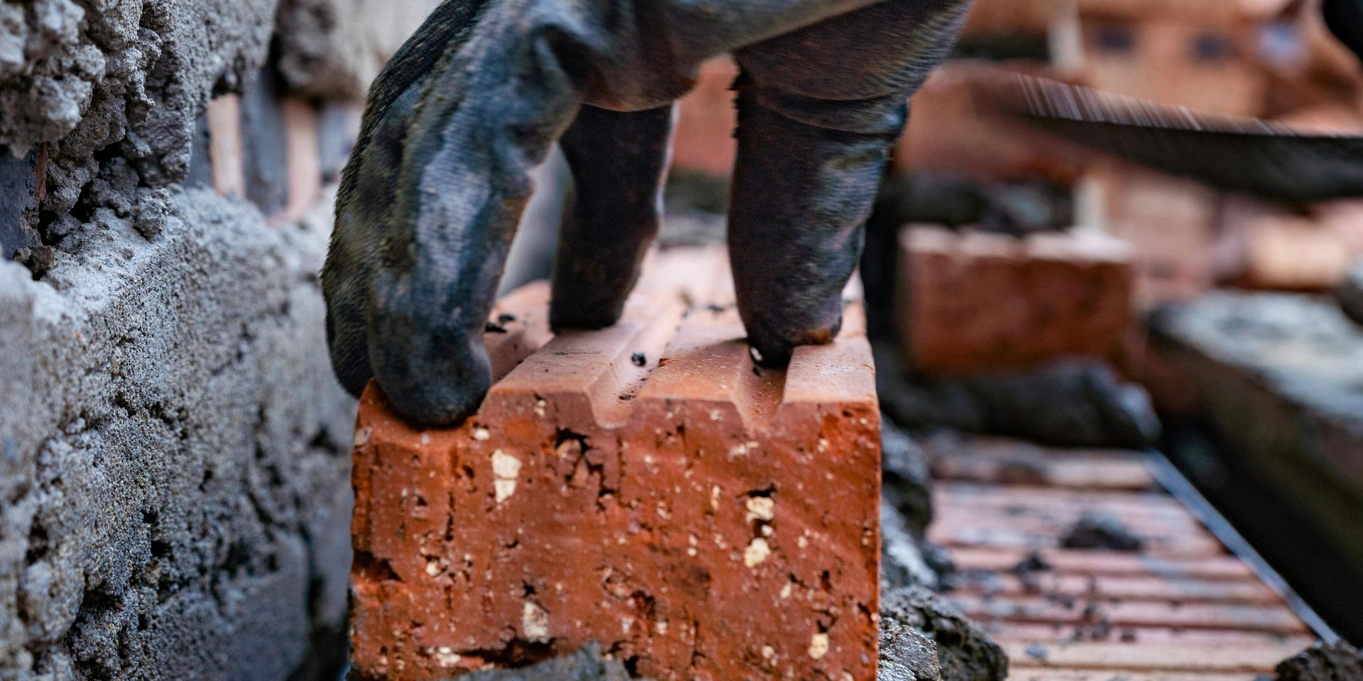 Bricklayer placing a brick on mortar, using a trowel and string line to build a wall.