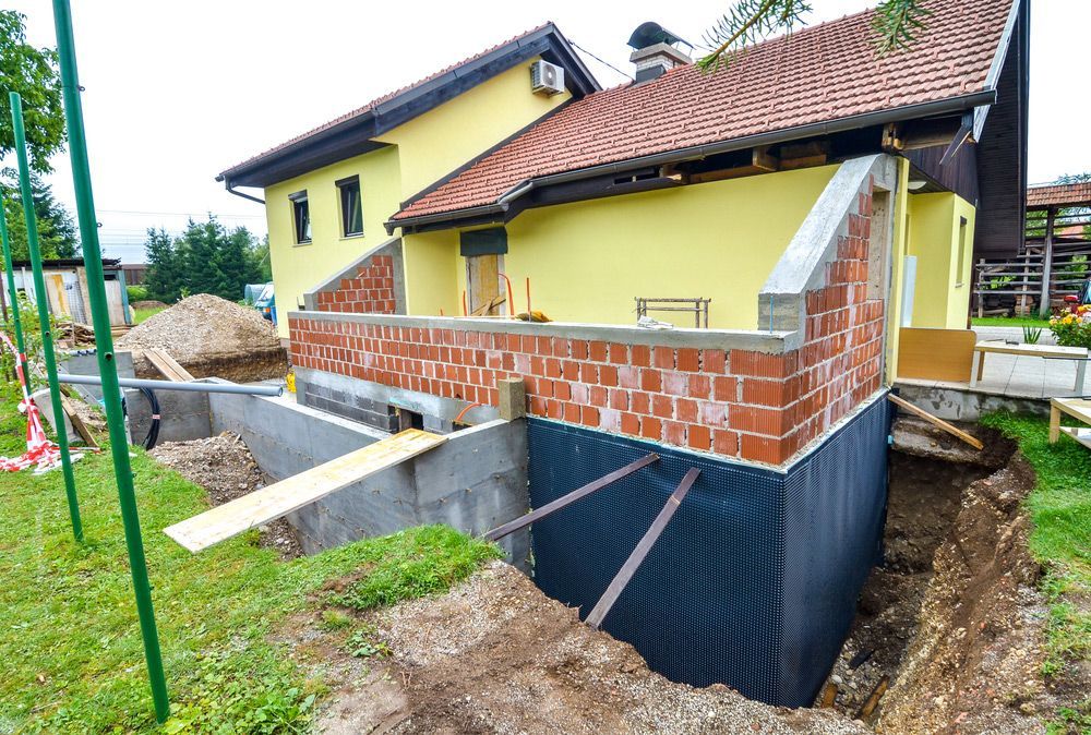 A yellow house is being built with a brick wall and a foundation.
