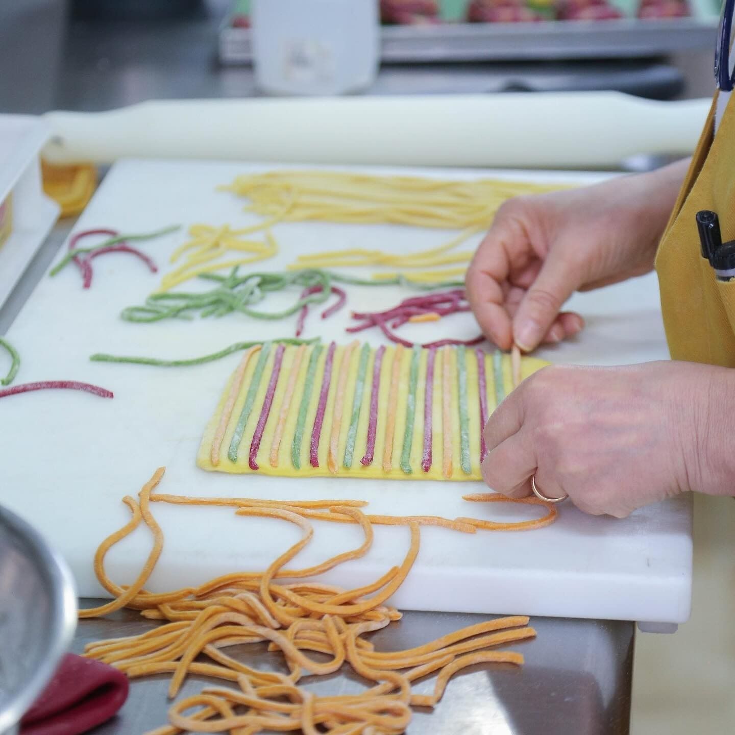 Persona che dispone su un tagliere bianco dei coloratissimi spaghetti di pasta fatti a mano.