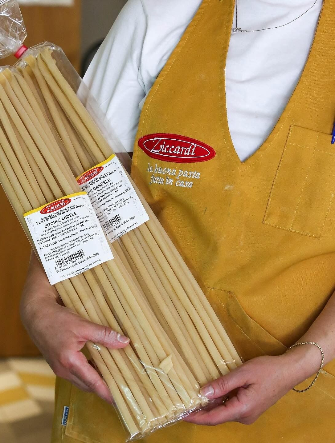 Persona che tiene in mano un pacchetto di bastoncini di pasta lunghi e spessi e indossa un grembiule giallo.
