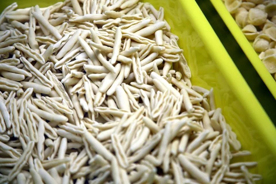Mucchio di cavatelli secchi, beige, in un bidone giallo, primo piano.