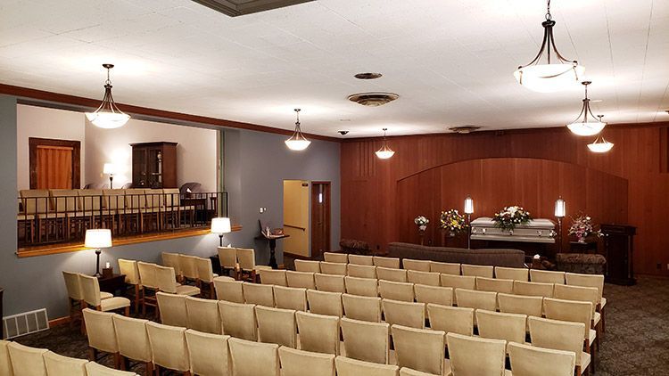 A large auditorium with rows of chairs and a coffin on the stage.