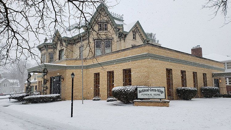 A large brick building with a sign in front of it is covered in snow.