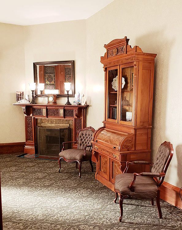 A living room with a fireplace , chairs , a desk and a hutch.